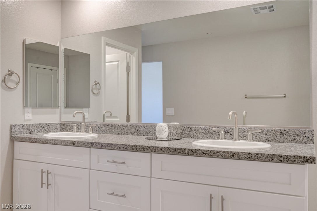 Double vanity with granite counters and white cabinetry creates a functional and pleasing bath.