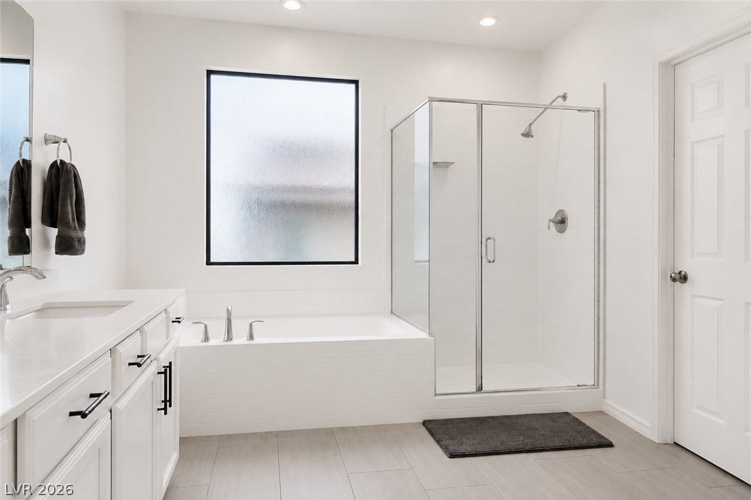 White walls and a large frosted window illuminate this elegant bathroom, featuring a modern tub and a glass-enclosed shower.