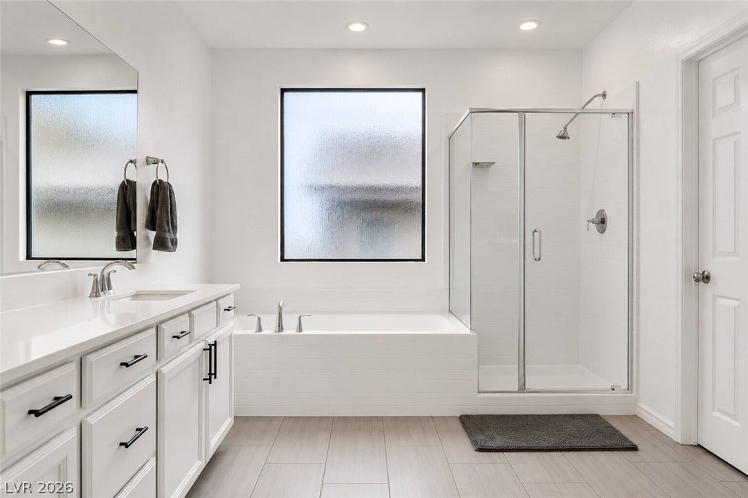 A well-appointed bathroom features a spacious soaking tub, a sleek glass-enclosed shower, and a pristine double vanity.