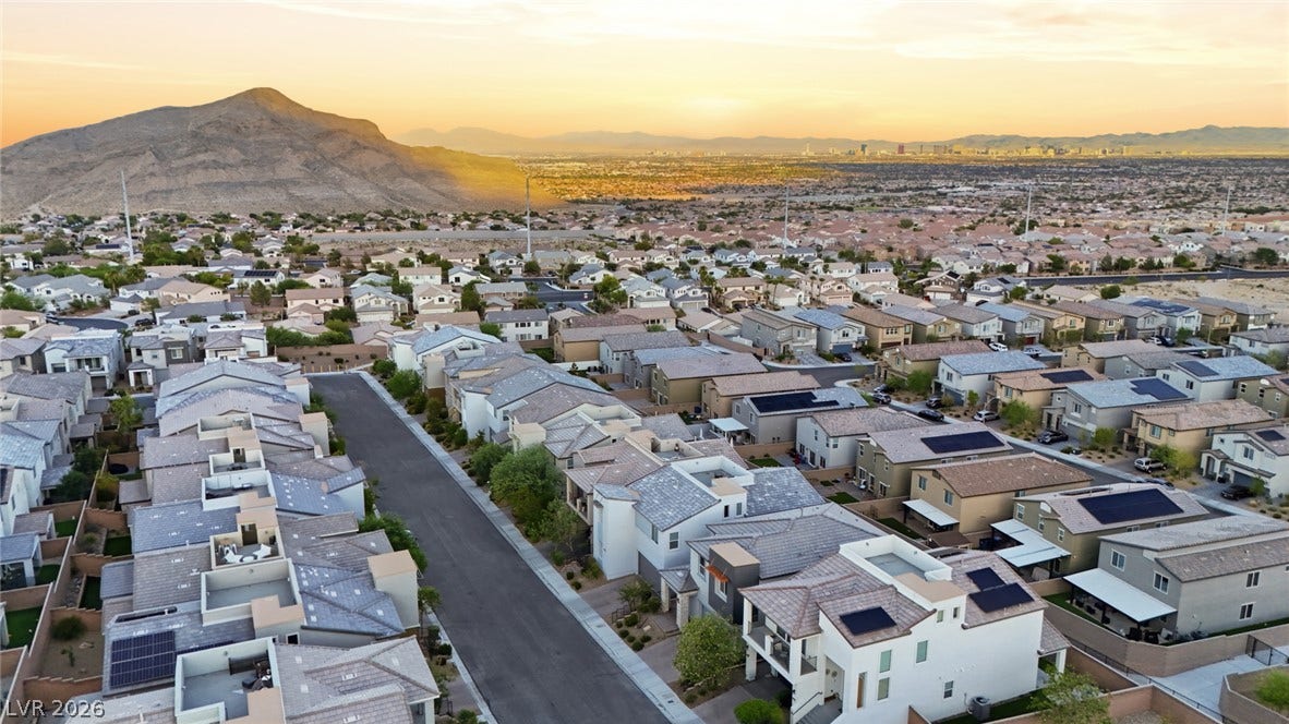 Aerial view captures a modern neighborhood nestled against a dramatic desert mountain backdrop at sunset.