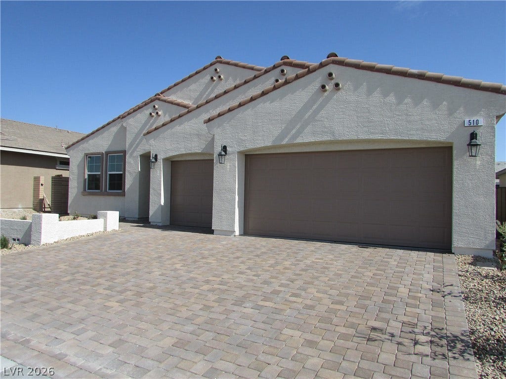 510 CHESTNUT FALCON AVE, Henderson, NV 89011 A paver driveway leads to a modern stucco home with a tile roof and integrated garage doors. Photo is Actual Home.