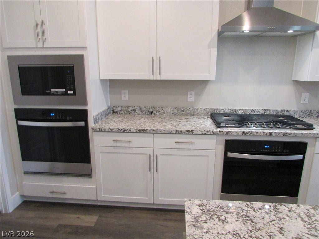 510 CHESTNUT FALCON AVE, Henderson, NV 89011 A contemporary kitchen features sleek white cabinetry, granite countertops, and stainless steel appliances.