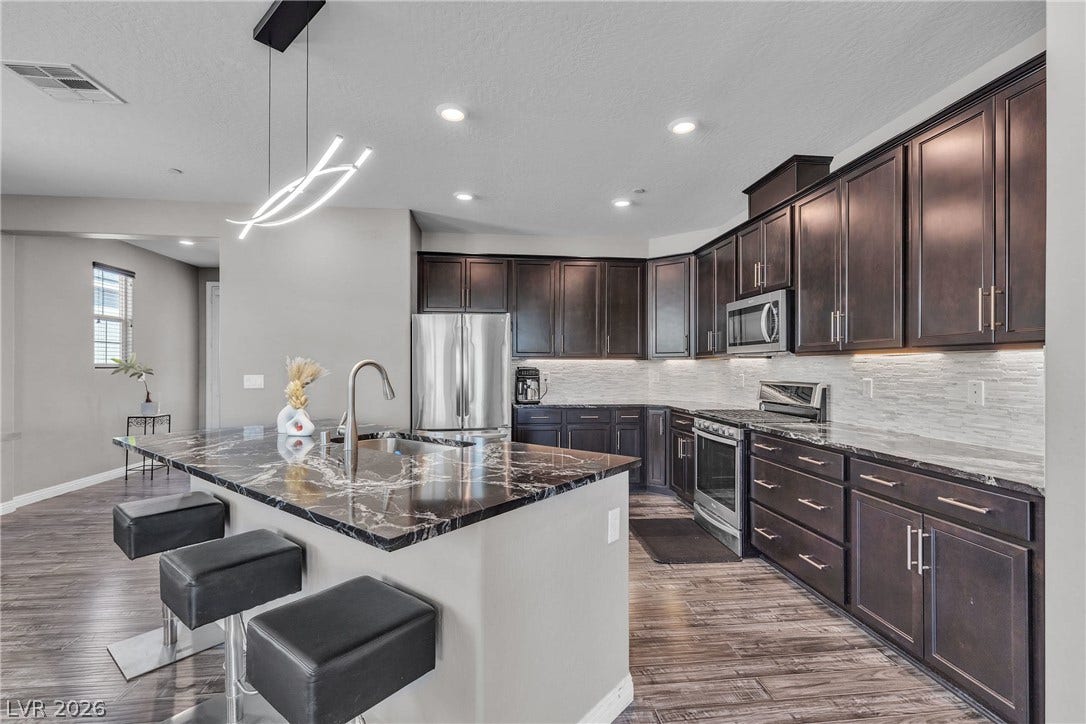 3106 Berceto Court, Henderson, NV 89044 An inviting kitchen features a central island with sleek black marble countertops and ample dark wood cabinetry.