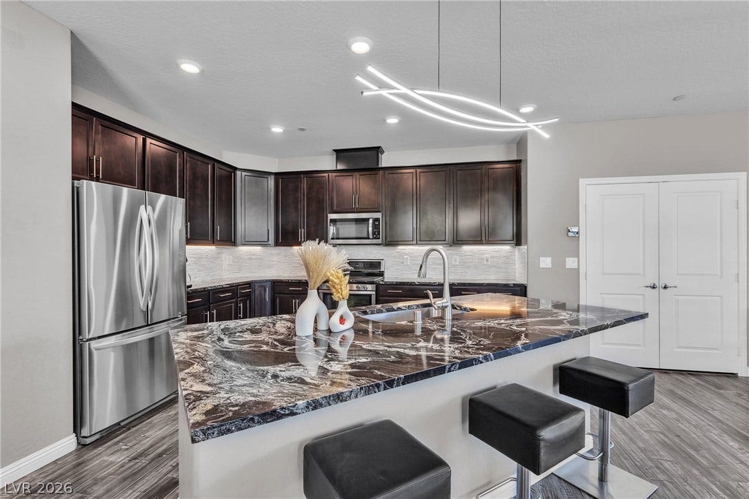 3106 Berceto Court, Henderson, NV 89044 Modern kitchen with deep-toned cabinetry, richly veined stone countertops, and sleek stainless steel appliances.