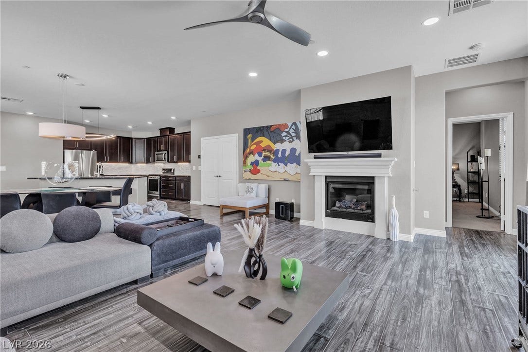 3106 Berceto Court, Henderson, NV 89044 An open concept living space features a modern fireplace, wood flooring, and a well-appointed kitchen beyond.