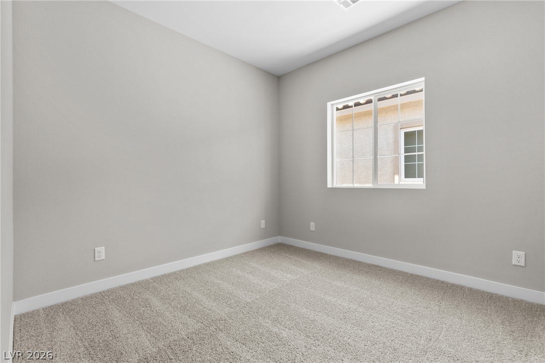 2405 Copperbelt Street, Las Vegas, NV 89030 A well-lit bedroom features plush carpeting and a bright window with views of a nearby structure.