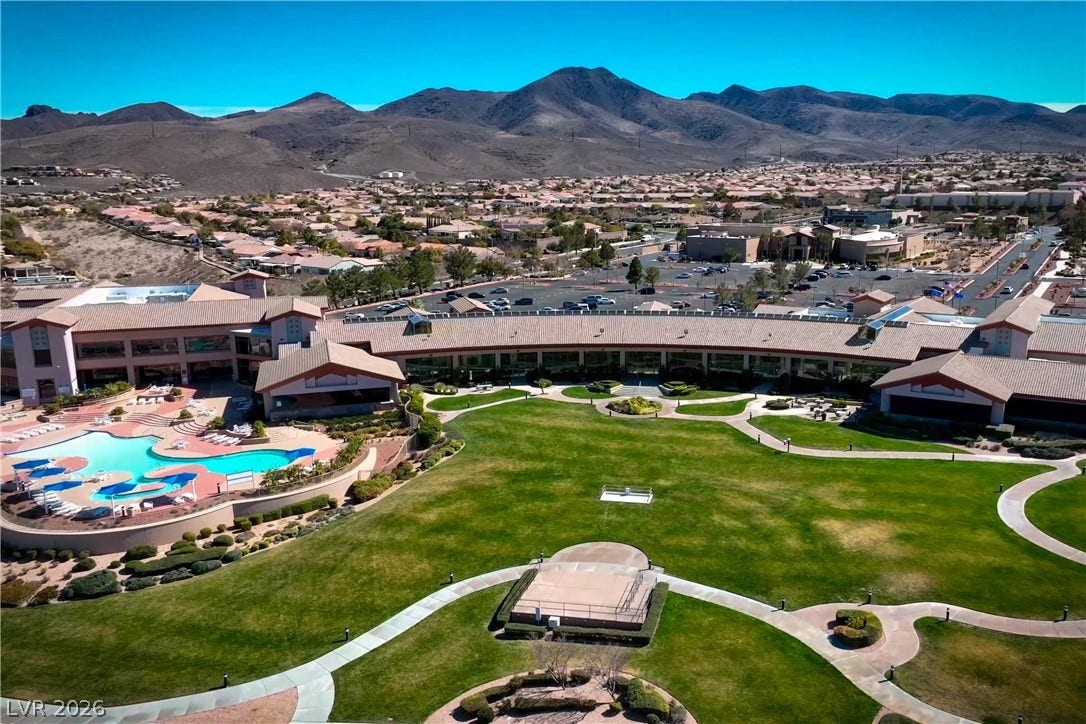 2157 Sawtooth Mountain Drive, Henderson, NV 89044 An aerial panorama reveals a vast green lawn, a large resort pool area, and mountain backdrops.