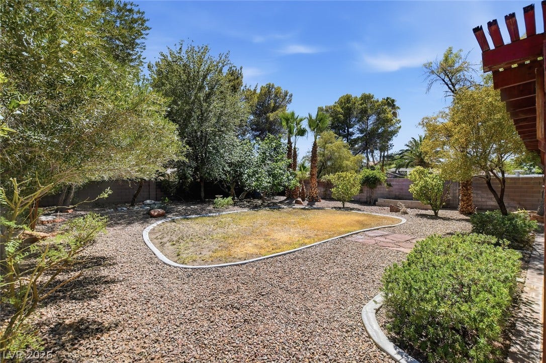 1827 Escondido Terrace, Henderson, NV 89074 A desert-friendly backyard featuring a gravel landscape with mature trees and a patch of natural grass.