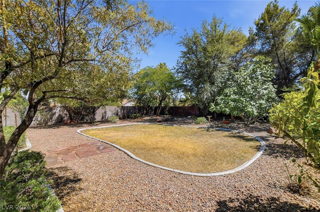 1827 Escondido Terrace, Henderson, NV 89074 A verdant backyard with mature trees and a gravel perimeter surrounds a central lawn.