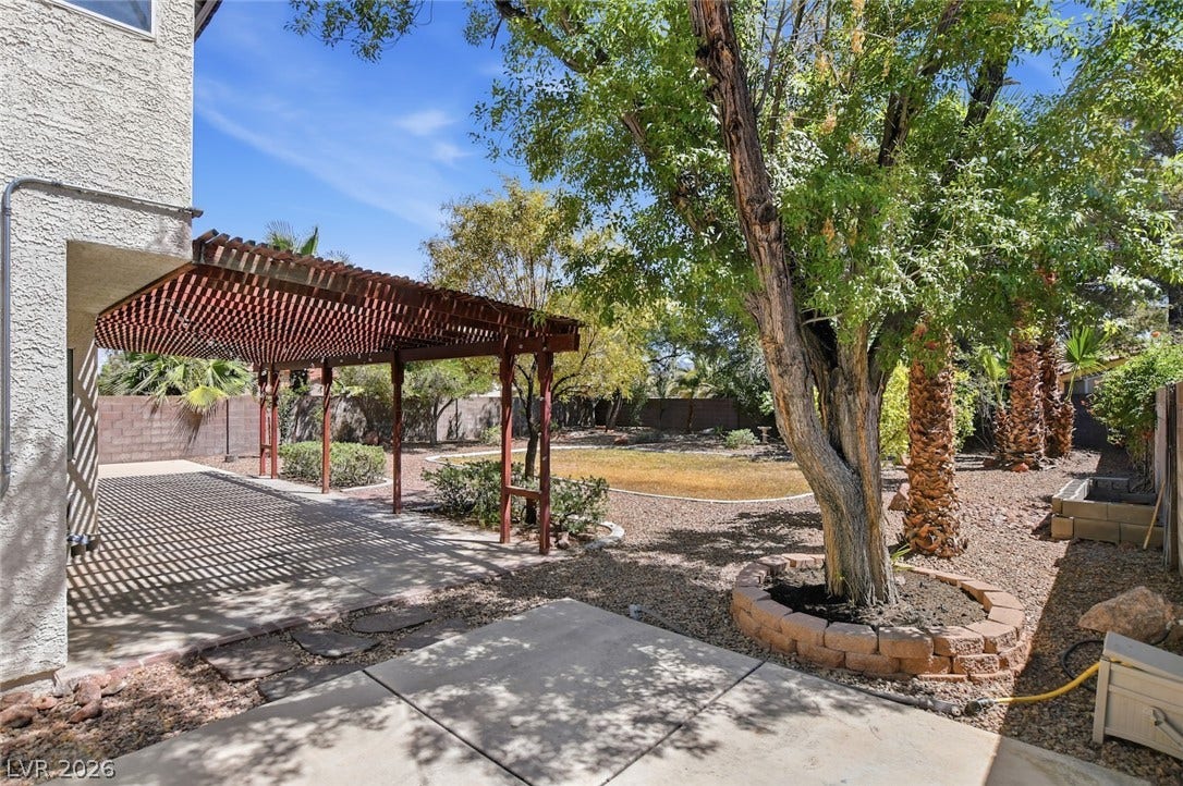 1827 Escondido Terrace, Henderson, NV 89074 An inviting backyard features a wooden pergola providing shaded patio space, adjacent to an open lawn area.