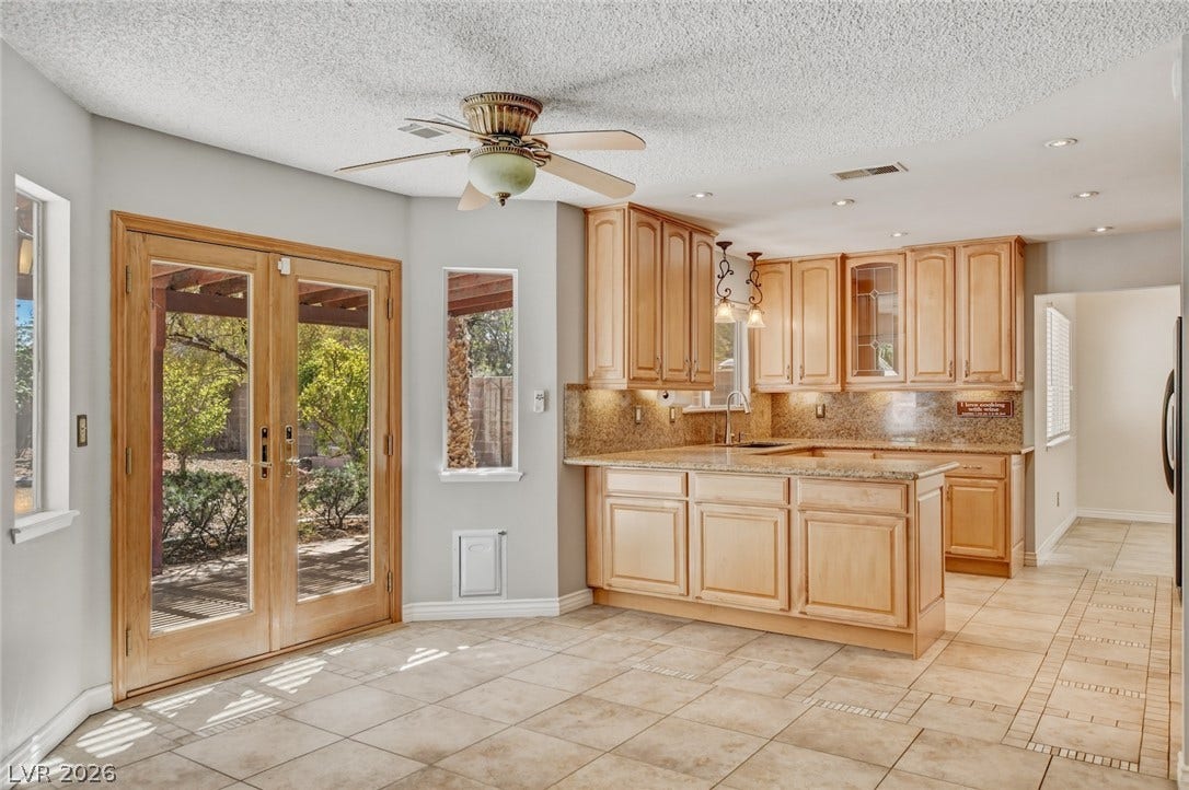 1827 Escondido Terrace, Henderson, NV 89074 A well-lit kitchen with natural wood cabinetry and a central island offers direct access to the outdoors through elegant French doors.