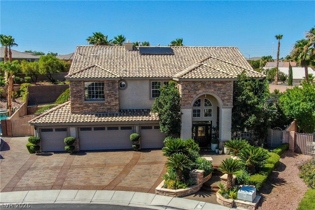 699 Brandy Hill Place, Henderson, NV 89052 Elegant two-story home with a tiled roof and intricate stone facade, boasting lush landscaping and a patterned driveway.