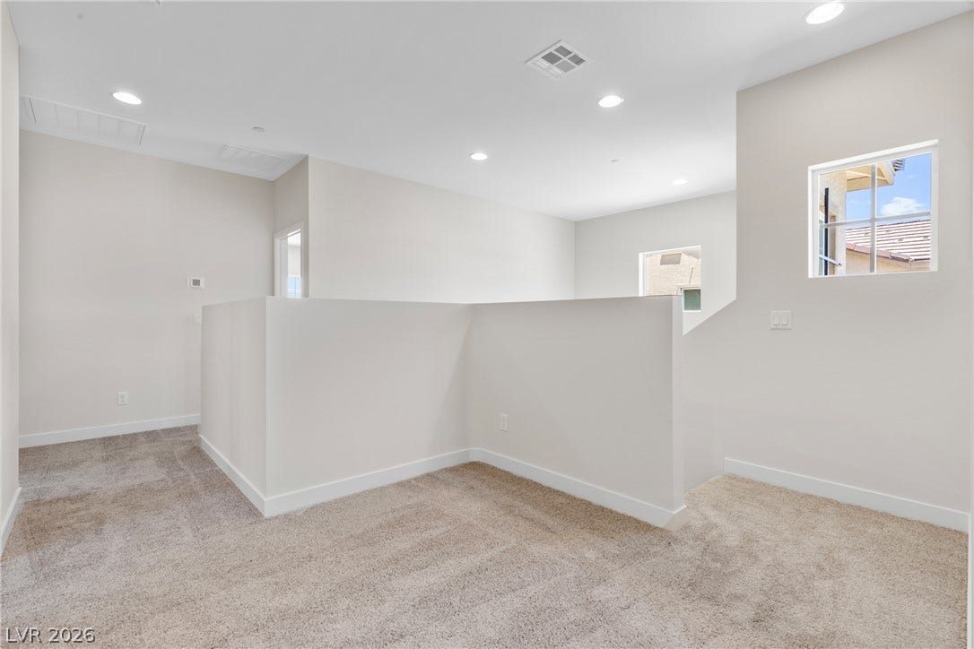 Recessed lighting illuminates this versatile upstairs landing featuring soft carpeting and clean lines.