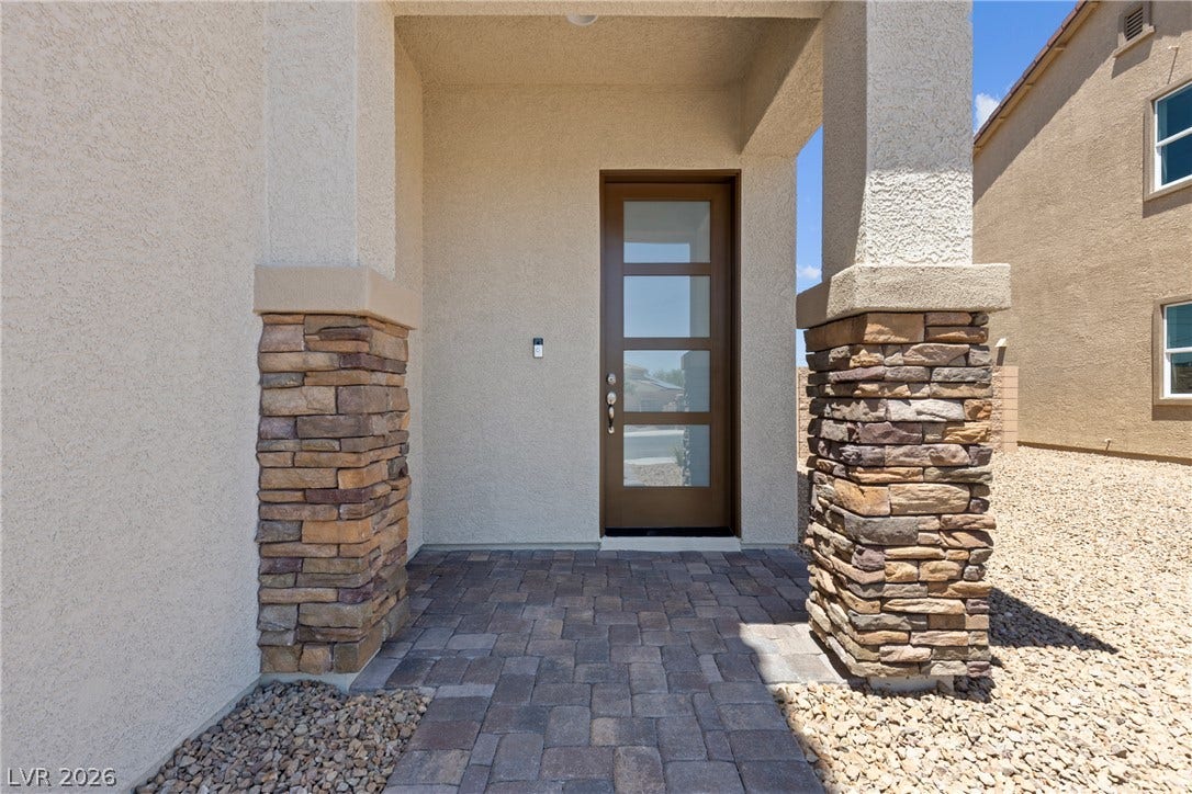 An inviting entryway features a modern glass-paneled door framed by robust stone pillars.