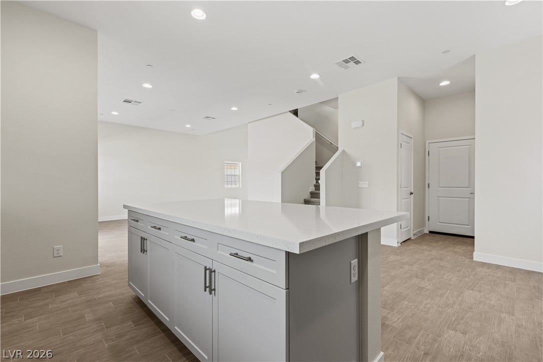 An open floorplan centers around a spacious kitchen island featuring stone counters and recessed lighting.