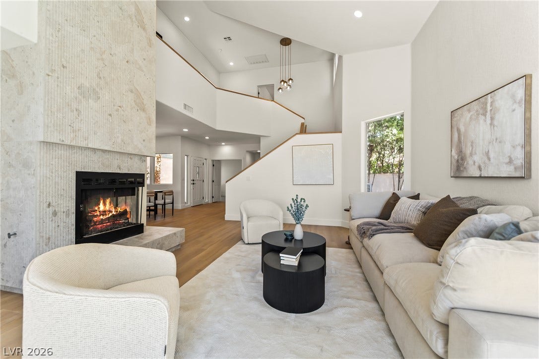 8921 Diamond Falls Drive, Las Vegas, NV 89117 A striking fireplace with a stone surround anchors this naturally illuminated living space, featuring high ceilings and warm wood flooring.