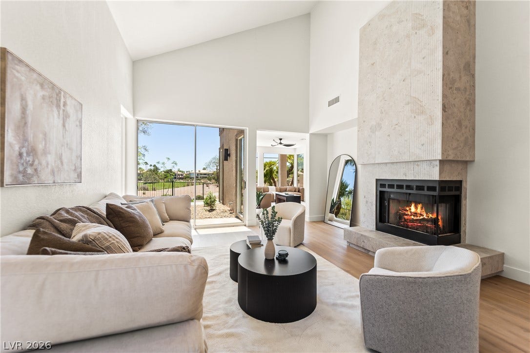 8921 Diamond Falls Drive, Las Vegas, NV 89117 A spacious living room features soaring ceilings and an elegant stone fireplace, opening to a private patio.