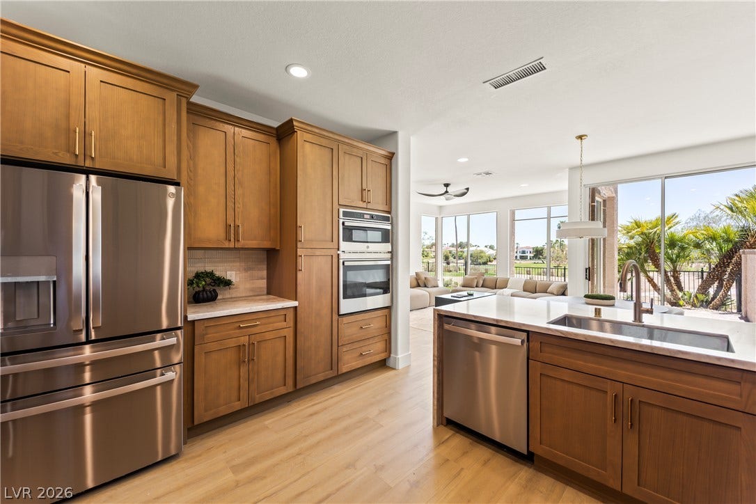 8921 Diamond Falls Drive, Las Vegas, NV 89117 A contemporary kitchen features warm wood cabinetry, stainless steel appliances, and a seamless flow into a sun-filled living area.