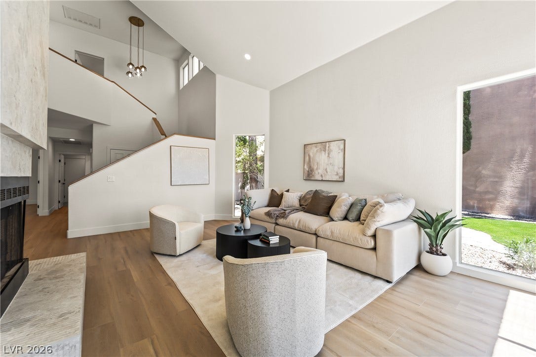8921 Diamond Falls Drive, Las Vegas, NV 89117 High ceilings and rich hardwood flooring define this open-concept living space, featuring a fireplace and large windows for natural illumination.