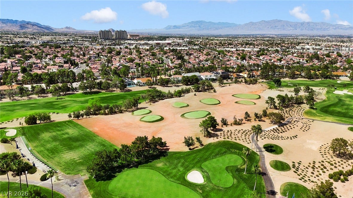 8921 Diamond Falls Drive, Las Vegas, NV 89117 Aerial view showcasing a lush green golf course interspersed with desert landscaping, surrounded by residential areas and distant mountains.