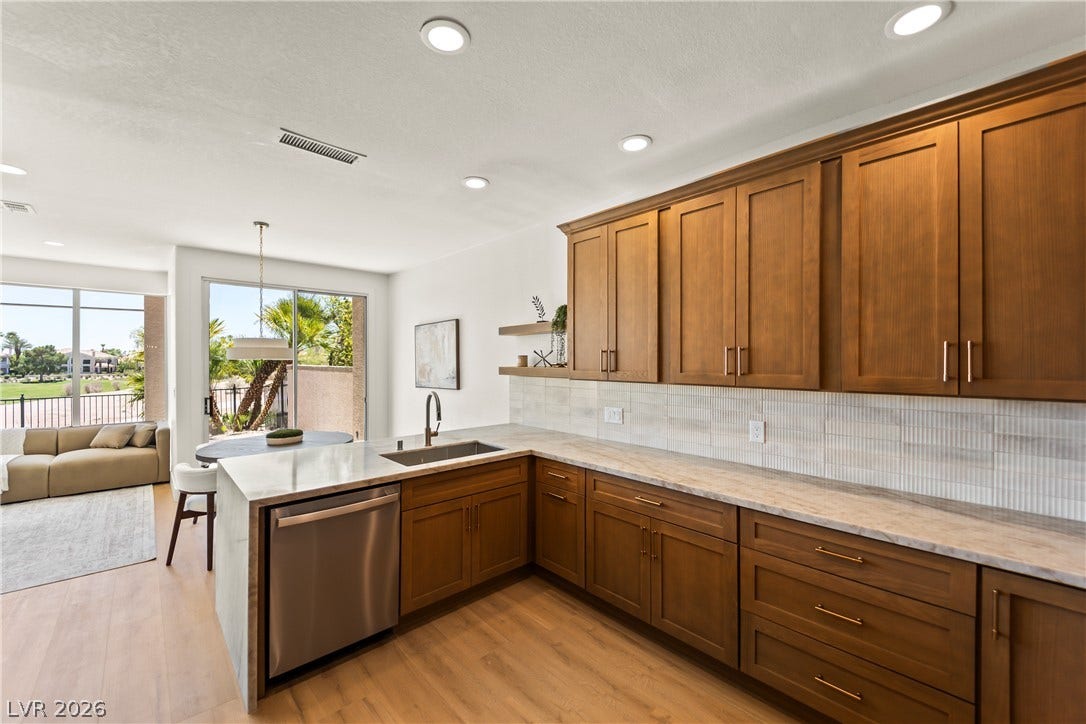 8921 Diamond Falls Drive, Las Vegas, NV 89117 A contemporary kitchen boasts wooden cabinetry, granite countertops, and seamless views of the outdoors through a sliding glass door.