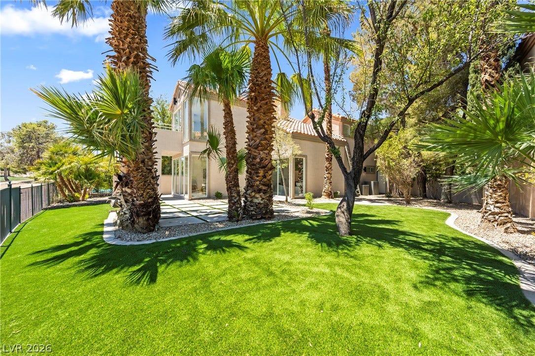 8921 Diamond Falls Drive, Las Vegas, NV 89117 A private yard with vivid green artificial turf and majestic palm trees framing the contemporary architecture.