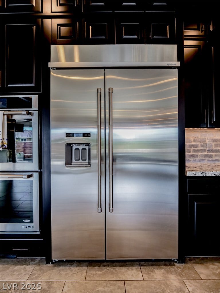 12013 Tramonto Avenue, Las Vegas, NV 89138 Dark cabinetry frames high-end stainless steel appliances and a brick backsplash above stone countertops.