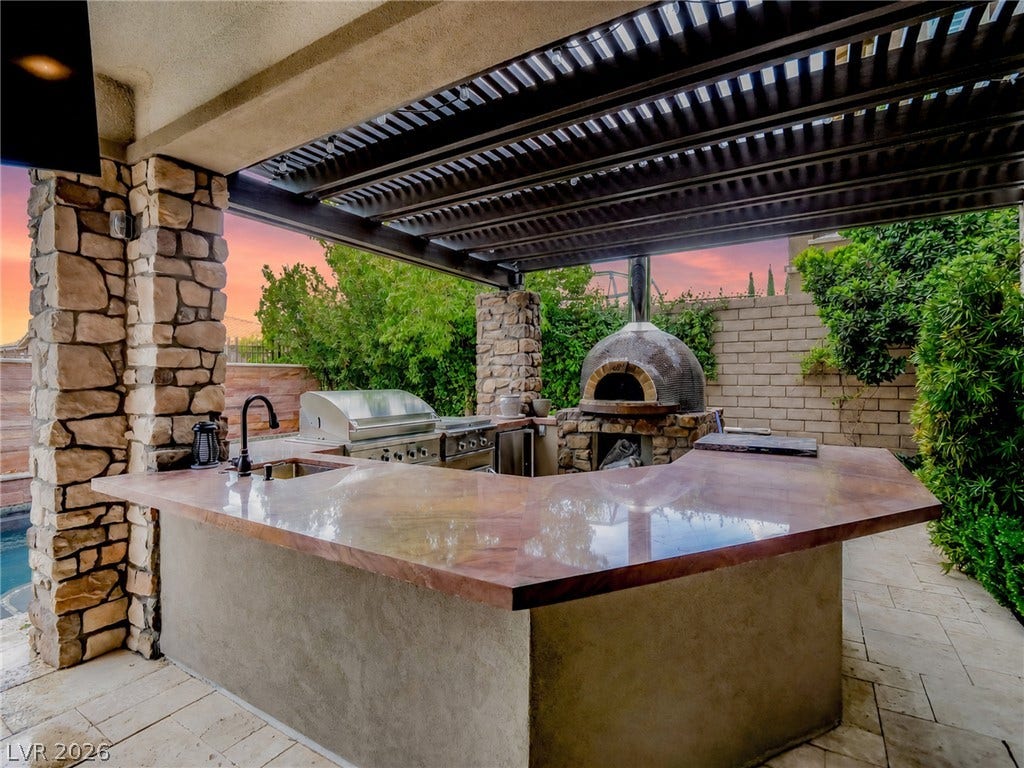 12013 Tramonto Avenue, Las Vegas, NV 89138 Stone pillars and a louvered pergola frame a fully equipped outdoor kitchen with custom countertops.