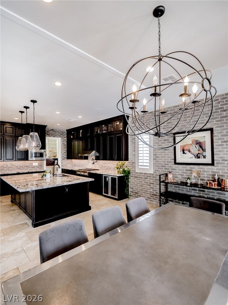 12013 Tramonto Avenue, Las Vegas, NV 89138 Exposed brick walls and dark cabinetry frame this open kitchen and dining area.