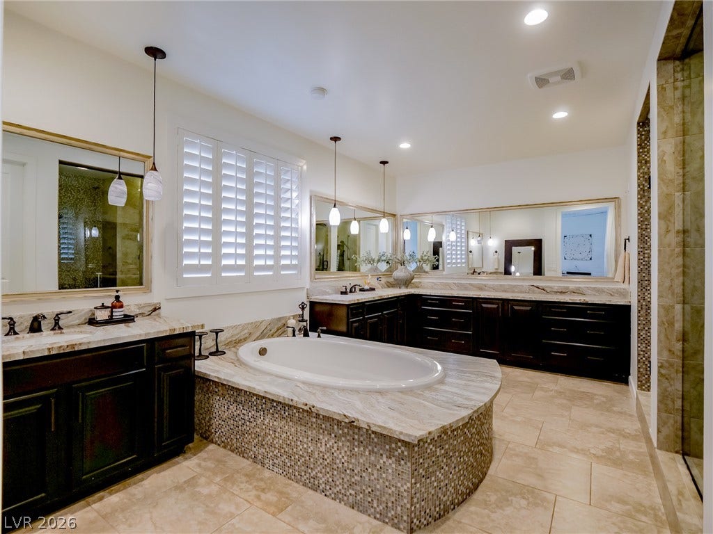 12013 Tramonto Avenue, Las Vegas, NV 89138 Rich wood vanities and stone surfaces surround a mosaic-accented soaking tub in this bathroom.