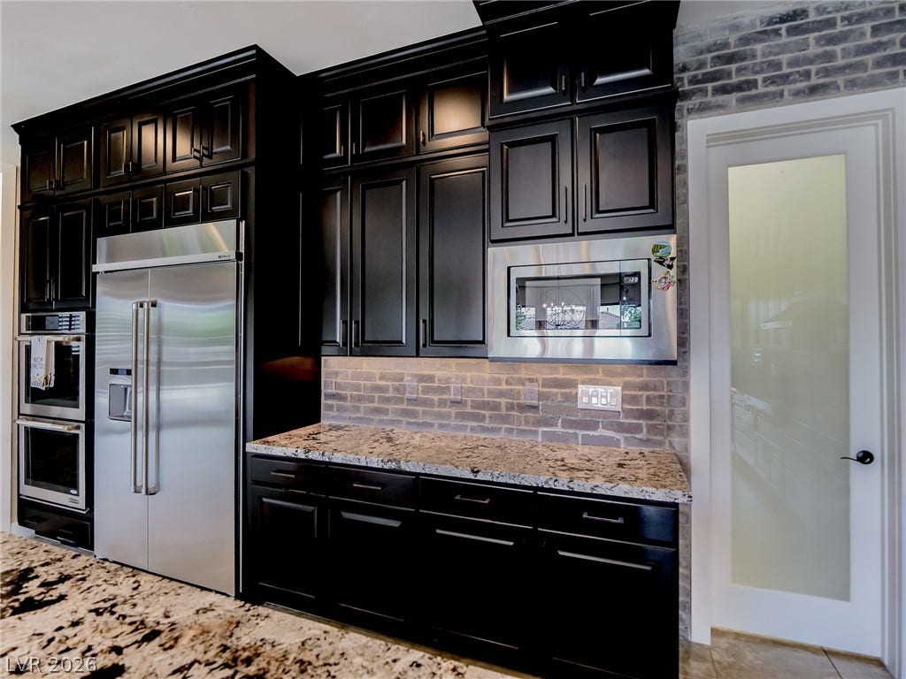 12013 Tramonto Avenue, Las Vegas, NV 89138 Dramatic dark cabinetry pairs beautifully with rich granite countertops and a classic brick backsplash.