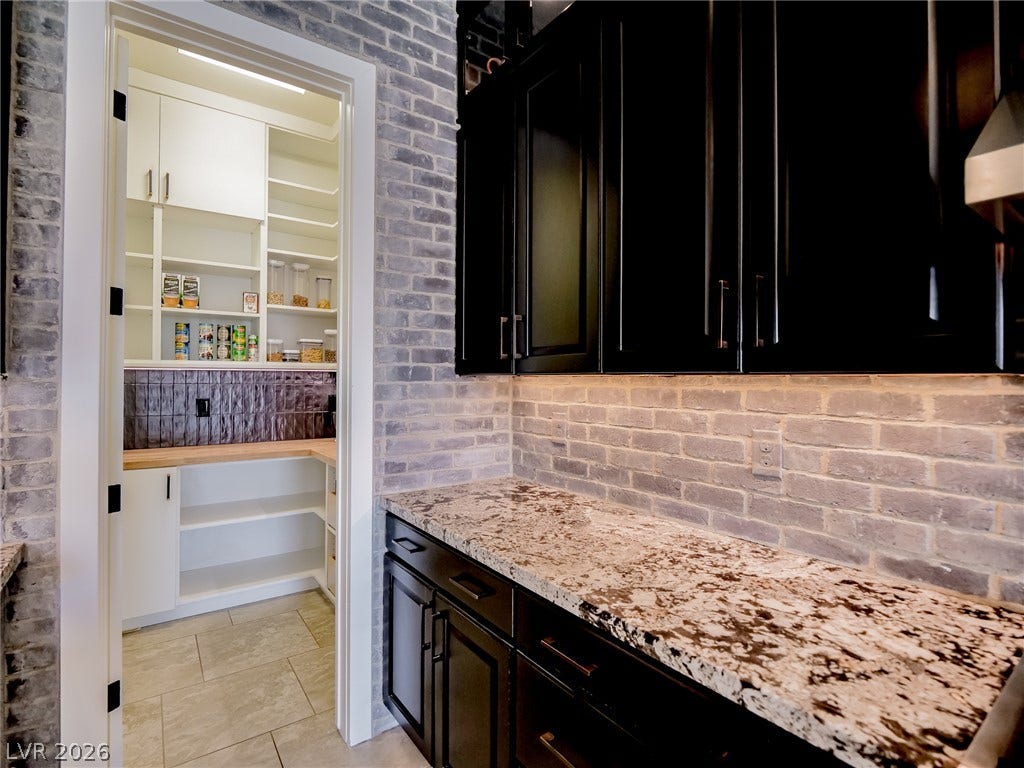 12013 Tramonto Avenue, Las Vegas, NV 89138 A walk-in pantry sits adjacent to granite countertops and brick accent walls.