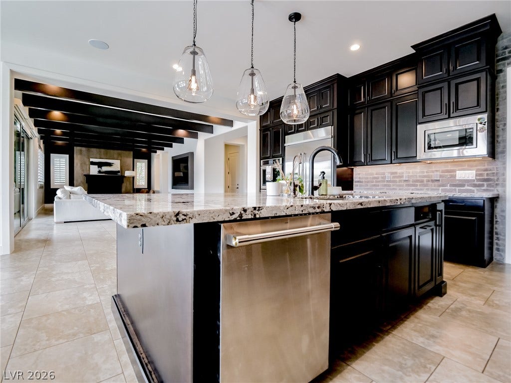 12013 Tramonto Avenue, Las Vegas, NV 89138 Gleaming stone countertops and dark cabinetry anchor this open-concept kitchen under recessed lighting.