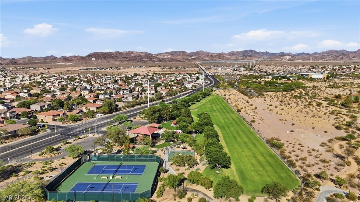 206 Oleander Place, Henderson, NV 89015 An aerial panorama reveals a vibrant green tennis court alongside a sprawling neighborhood with distant mountain views.