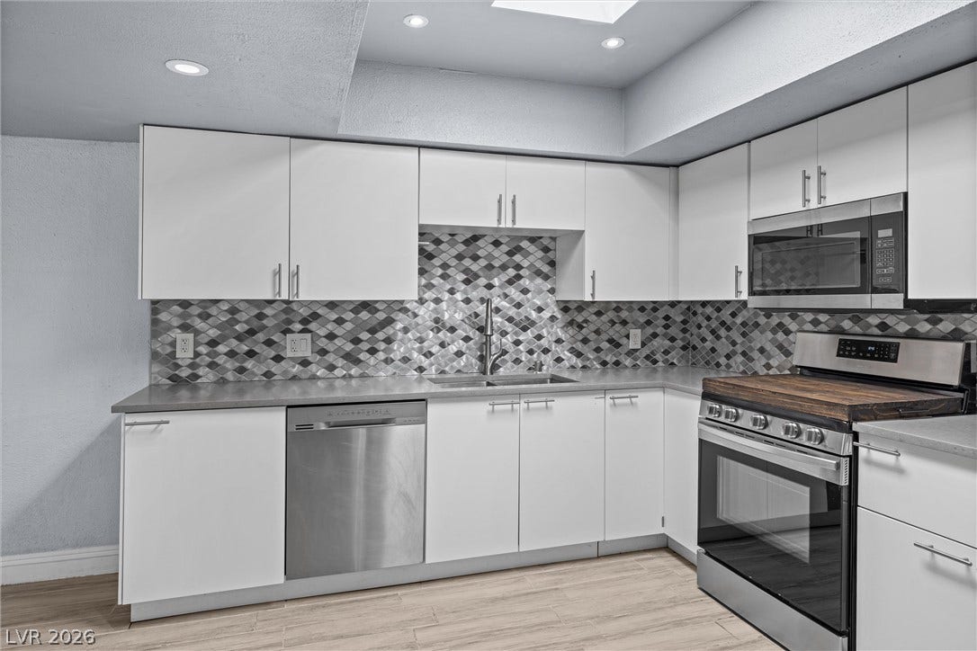 3303 Royce Court, Las Vegas, NV 89121 A streamlined kitchen design features sleek white cabinetry and modern stainless steel appliances.