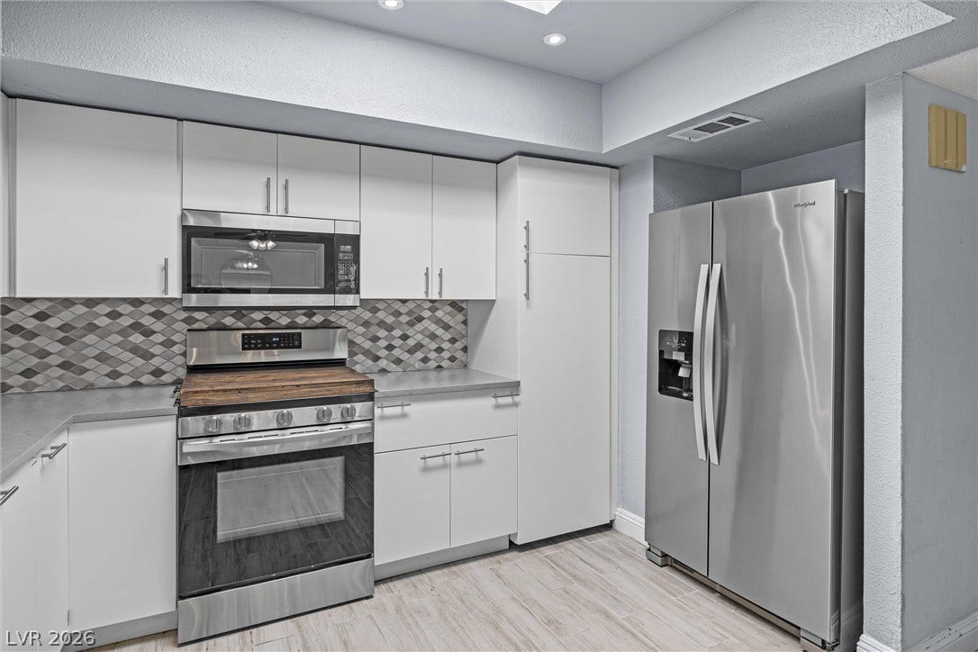 3303 Royce Court, Las Vegas, NV 89121 A contemporary kitchen features sleek white cabinetry, stainless steel appliances, and a stylish tiled backsplash.