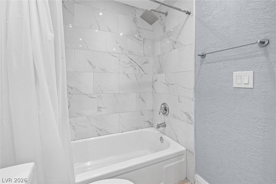 3303 Royce Court, Las Vegas, NV 89121 A pristine bathroom features a classic soaking tub and contemporary marble-patterned tile shower surround.