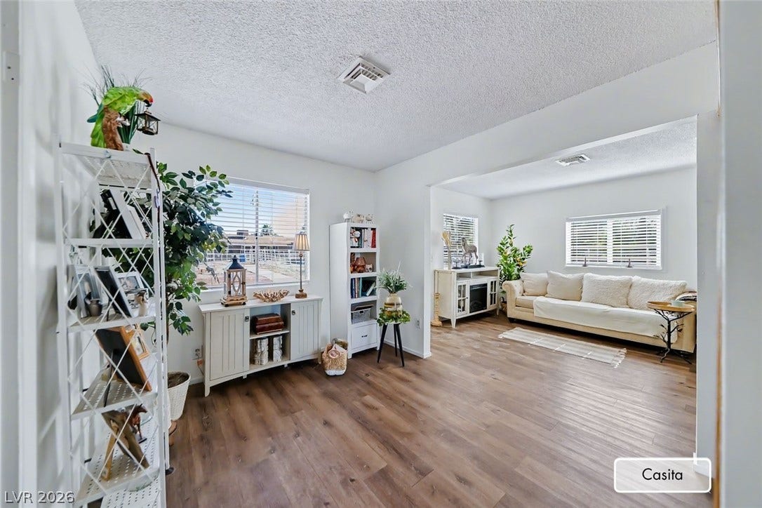 Rich wood-look flooring anchors this open guest house living area illuminated by multiple windows.