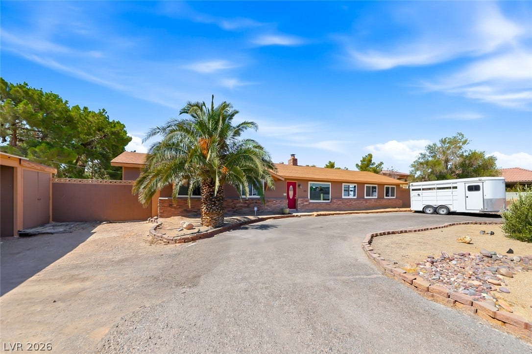 A gracefully horseshoe driveway guides to this welcoming desert ranch home with mature palm trees.