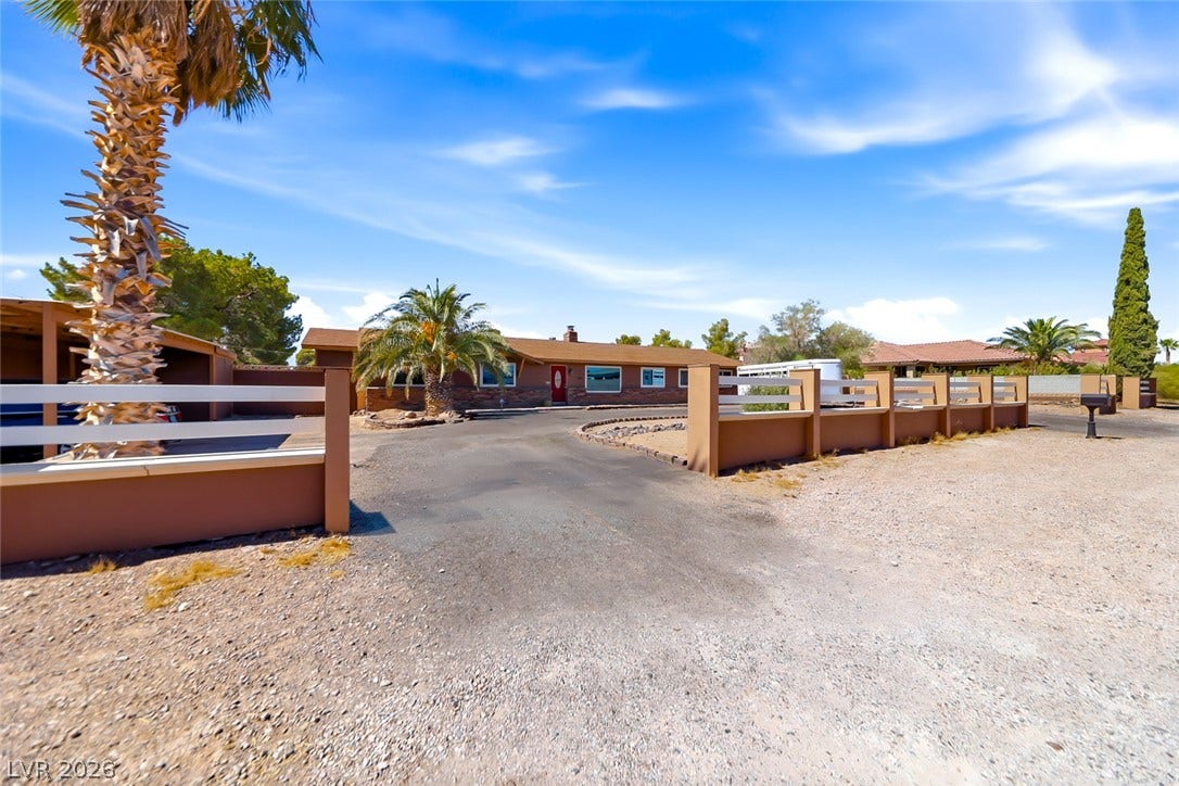 A horseshoe driveway leads to this single-story ranch home with desert landscaping and a welcoming red door.