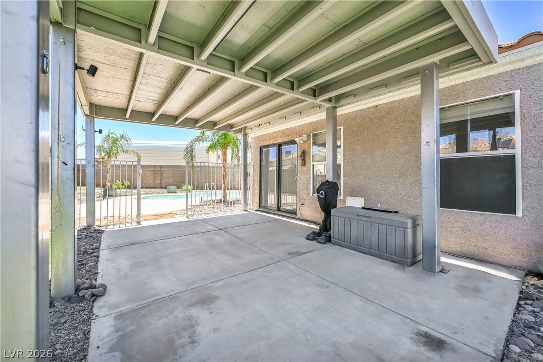 A spacious covered patio provides a shaded oasis overlooking the sparkling pool and desert-inspired landscape.