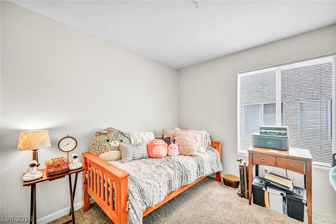 A well-lit bedroom features plush carpeting and a large window providing ample natural light.