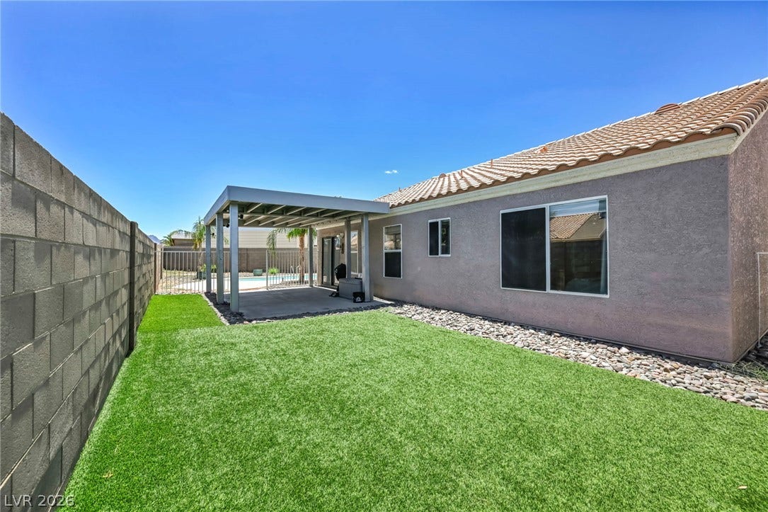 A well-maintained synthetic lawn and covered patio create an inviting outdoor living space.