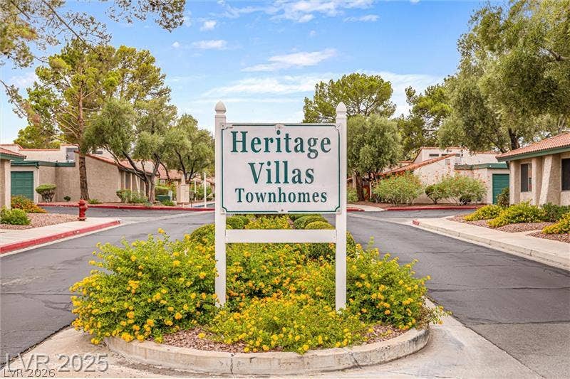 A welcoming sign marks the entrance to Heritage Villas Townhomes, surrounded by vibrant yellow flora and mature trees.