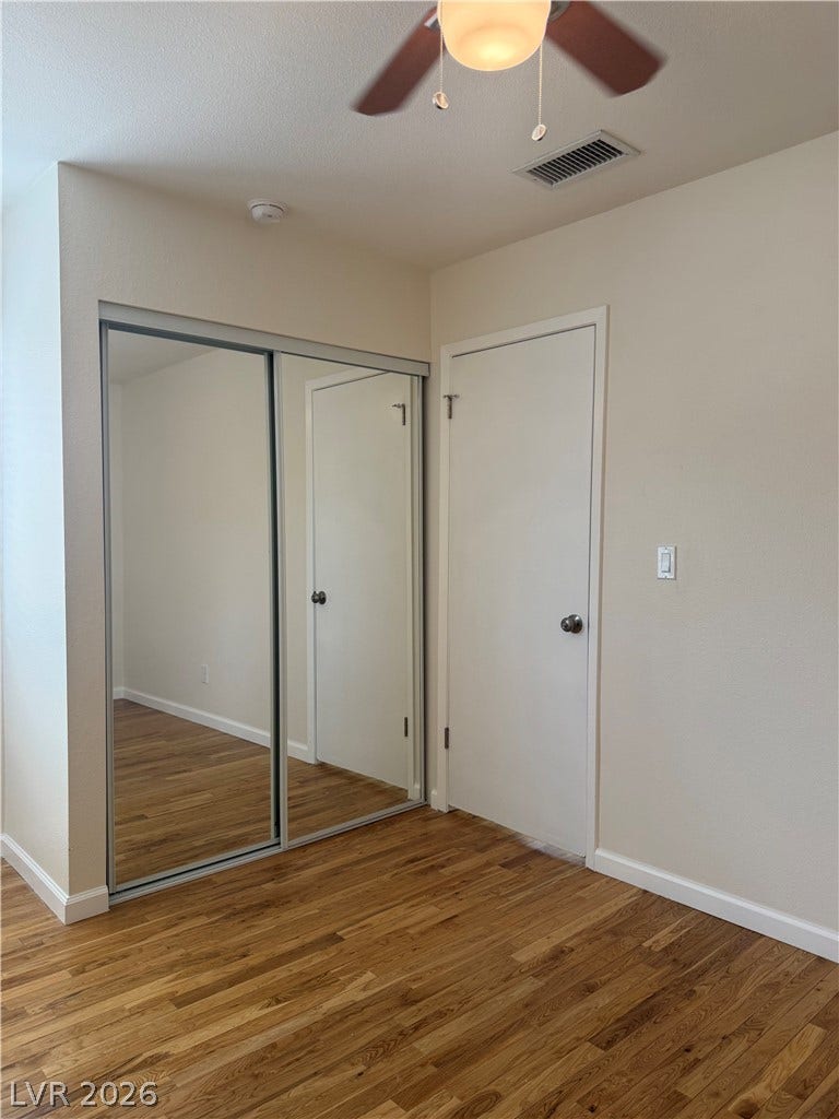 Hardwood floors and mirrored closet doors enhance this cozy bedroom, complete with a ceiling fan.