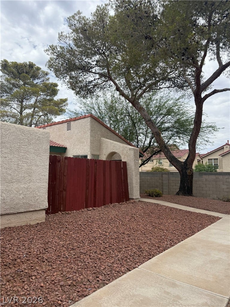 Mature trees frame a cozy residence, featuring a sturdy red fence and practical rock landscaping.