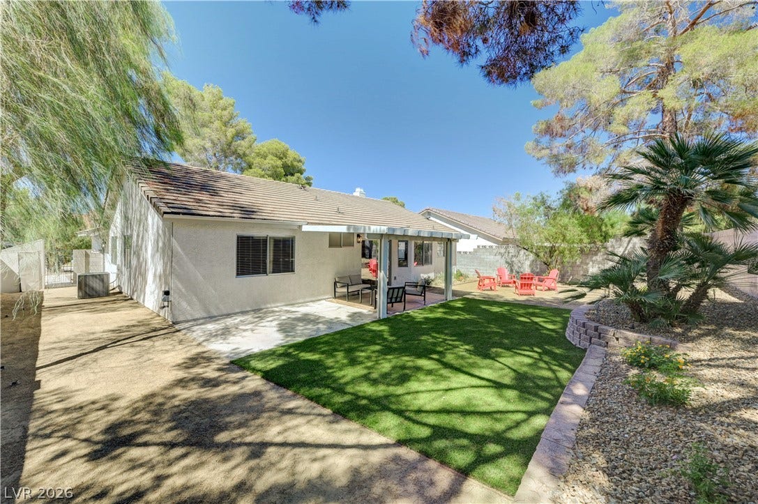 3131 White Rose Way, Henderson, NV 89014 A well-maintained outdoor space with synthetic turf, a shaded patio, and mature trees for serene relaxation.