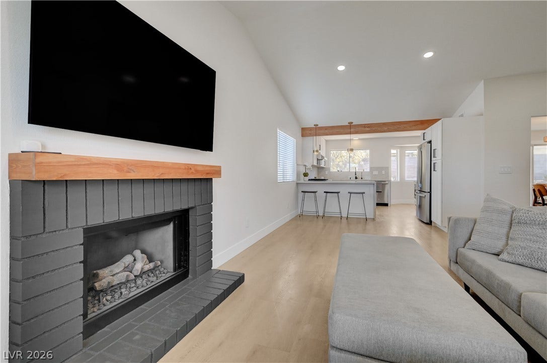 3131 White Rose Way, Henderson, NV 89014 A striking gray brick fireplace anchors this inviting open-concept living space with sleek hardwood flooring.