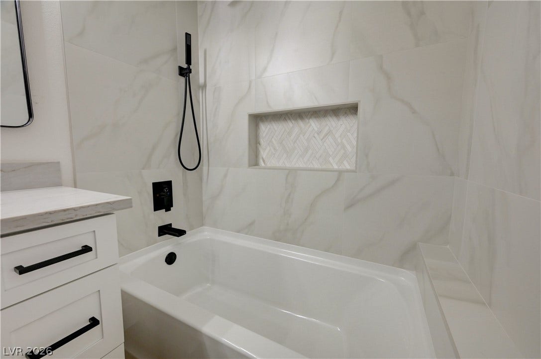 3131 White Rose Way, Henderson, NV 89014 A well-appointed bathroom features a deep soaking tub and elegant marble-patterned wall tiling.