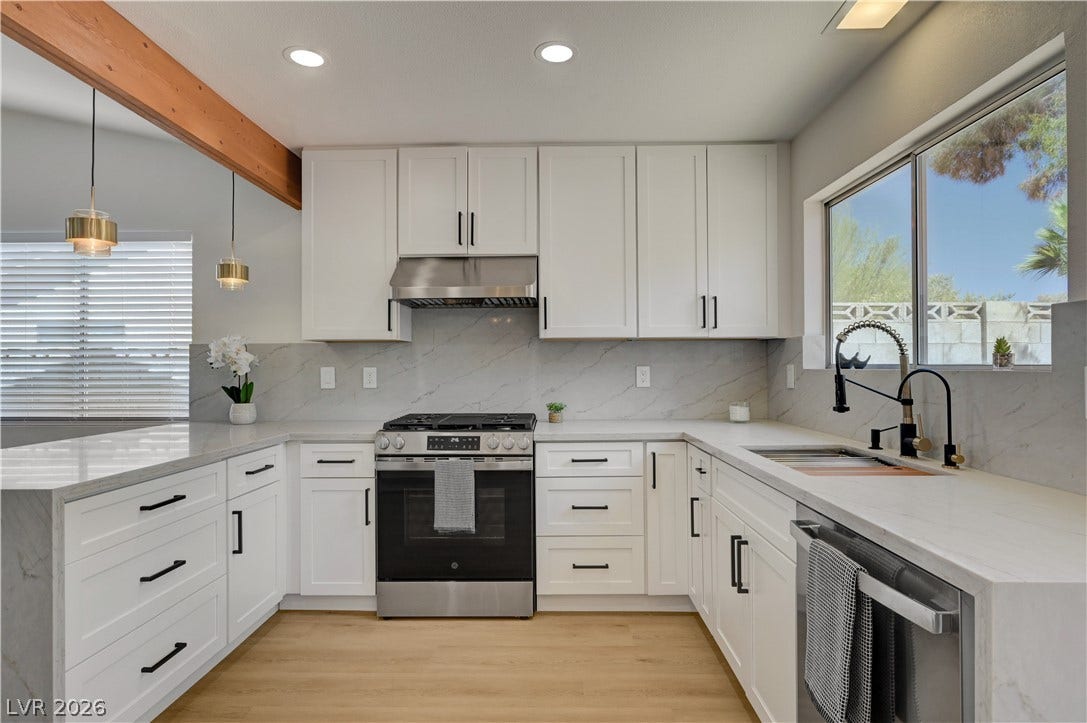 3131 White Rose Way, Henderson, NV 89014 A contemporary kitchen boasts pristine white cabinetry, light countertops, and a full suite of stainless steel appliances.